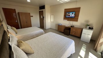 A hotel room with two beds, a desk, a refrigerator, and a television on the wall.