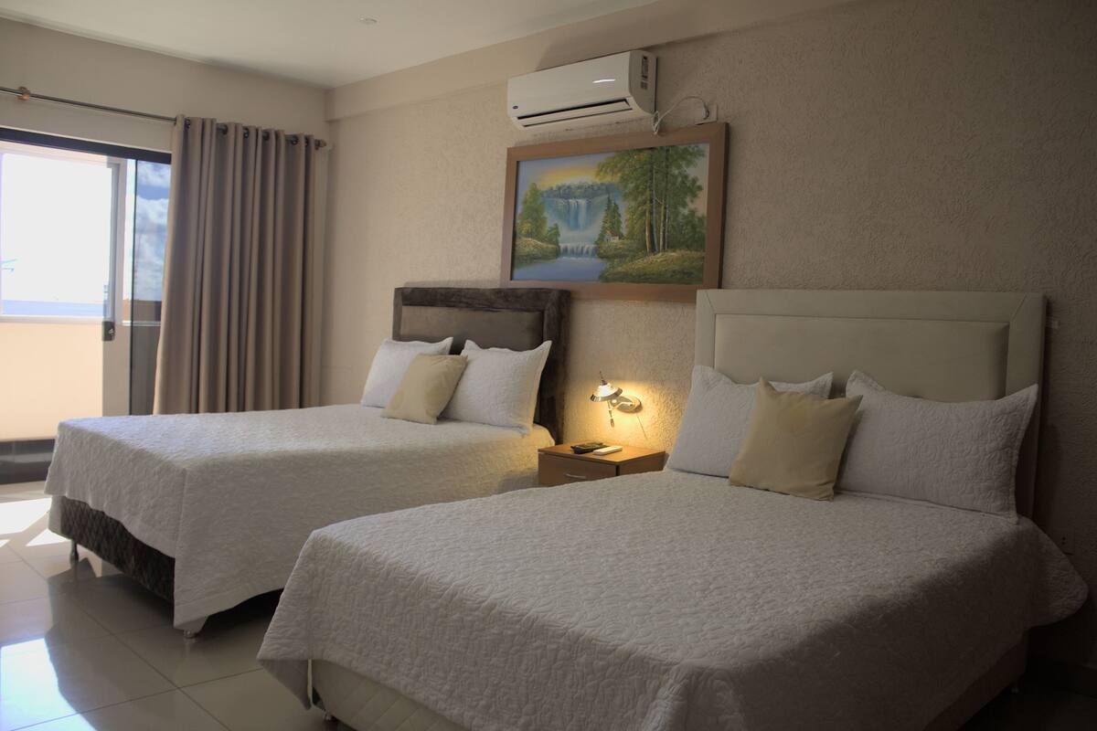 A hotel room with two beds, a painting on the wall, and an air conditioning unit.