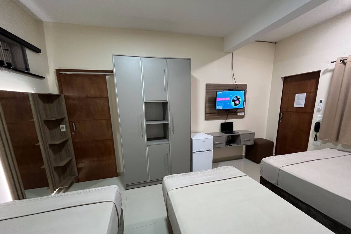 A hotel room with two beds, a wardrobe, a desk with a computer, a refrigerator, and a television on the wall.