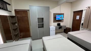 Habitación de hotel con dos camas, un armario, un escritorio con computadora, un refrigerador y un televisor en la pared.