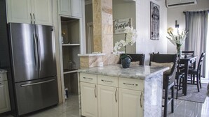 Una cocina con refrigerador de acero inoxidable, encimeras de mármol y una zona de comedor con sillas y una mesa.