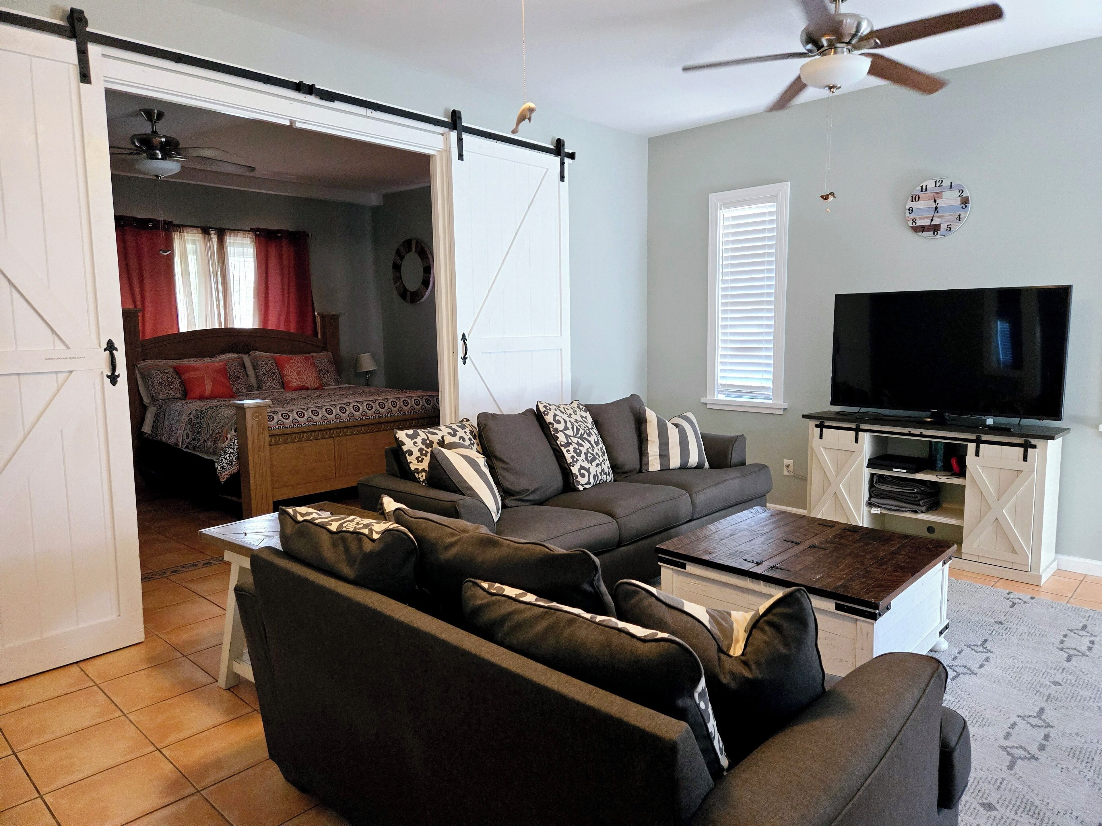 A living room with a sofa, coffee table, TV, and a sliding door leading to a bedroom.
