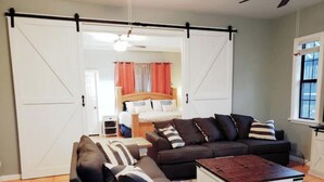 Uma sala de estar com um sofá, uma mesa de centro e uma porta deslizante que dá para um quarto.