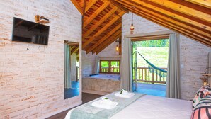Ein Schlafzimmer mit einem großen Bett, Holzboden, Mauerwerkwand und Blick auf einen Garten.