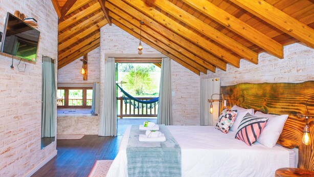 Ein Schlafzimmer mit Holzboden, einem Bett mit Kissen, einem Nachttisch und Blick auf eine Hängematte draußen.