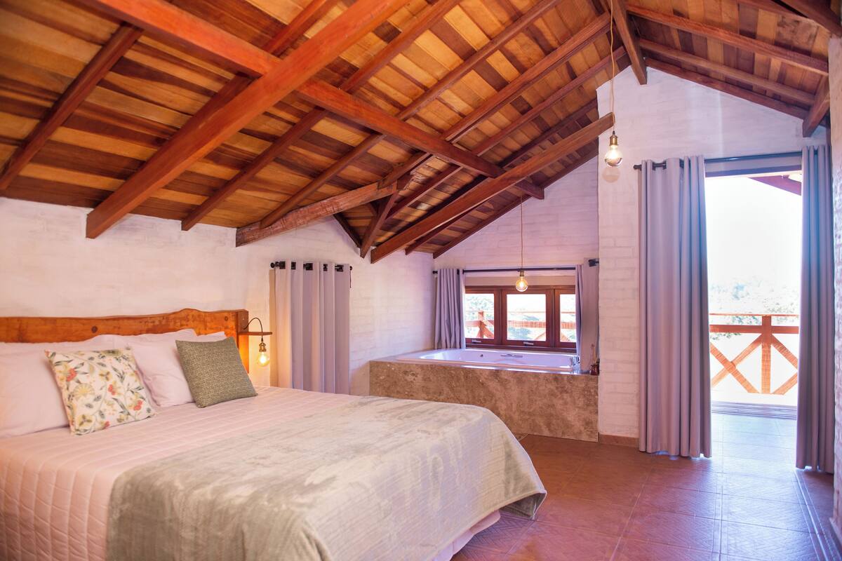 Une chambre avec un plafond en bois, un grand lit, une fenêtre avec des rideaux et une vue sur l’extérieur.