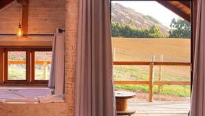 Ein Zimmer mit Holzböden, einem großen Fenster mit Vorhängen, einer hölzernen Bank und Blick auf eine Hügellandschaft.