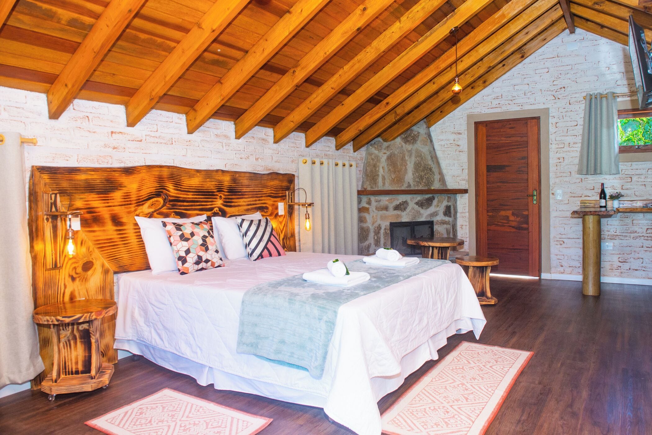 A bedroom with a large bed, wooden headboard, and a stone fireplace.