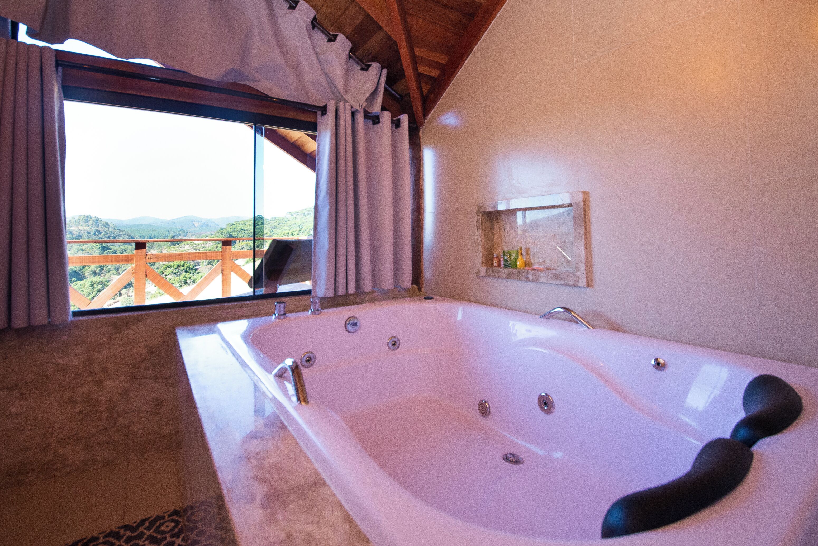 Un baño con una bañera grande, vistas a las montañas a través de una ventana y un balcón de madera afuera.