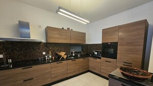 A modern kitchen with dark wood cabinets, a black countertop, and a tiled backsplash.