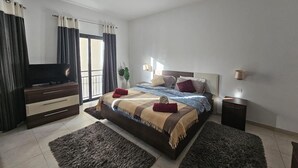 A modern bedroom with a large bed, a flat-screen TV, a dresser, and a small table.
