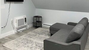 Una sala de estar moderna con un sofá gris, un televisor de pantalla plana montado en la pared, un radiador blanco y una pequeña mesa redonda.