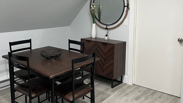 Un comedor con una mesa y sillas de madera, un armario pequeño y un espejo redondo en la pared.