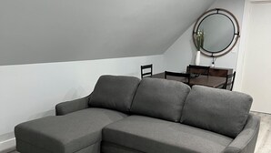 Un sofá seccional gris con un reposapiés a juego en una habitación con techo blanco y un espejo redondo en la pared.