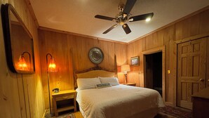 A bedroom with wooden paneling, a bed with white bedding, a ceiling fan, and a nightstand with a lamp. - Charming 1-bedroom apartment in Oxford (Oxford)