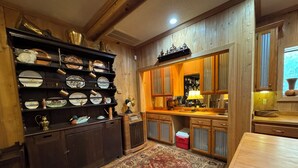 A traditional kitchen with wooden cabinets, a built-in shelf with dishes, a patterned rug, and a window with curtains. - Charming 1-bedroom apartment in Oxford (Oxford)
