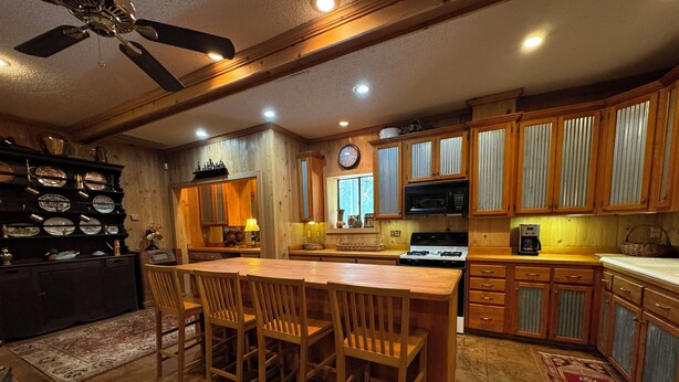 A kitchen with wooden cabinets, a central island with chairs, a stove, and a microwave. - Charming 1-bedroom apartment in Oxford (Oxford)