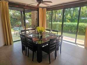 Enjoy meals in this dining area with a glass-top table and six chairs, surrounded by a lush garden view.