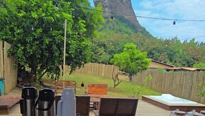 A dining table with various food items and condiments, set against a backdrop of a lush garden and a prominent rock formation. - Casa Pé na Areia (Fernando de Noronha)