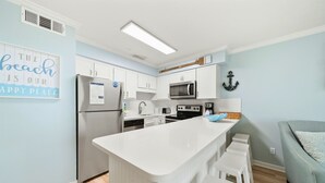 A modern kitchen with white cabinetry, a stainless steel refrigerator, a microwave, and a central island with bar stools. - 60 Secs to [Private] Beach Seagrove - Gulf views! (Seagrove)