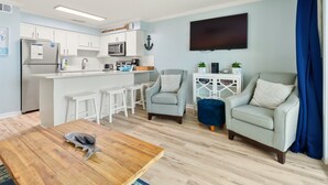 A modern living room with a wooden coffee table, two armchairs, a TV, and a kitchen area with white cabinets and a microwave. - 60 Secs to [Private] Beach Seagrove - Gulf views! (Seagrove)