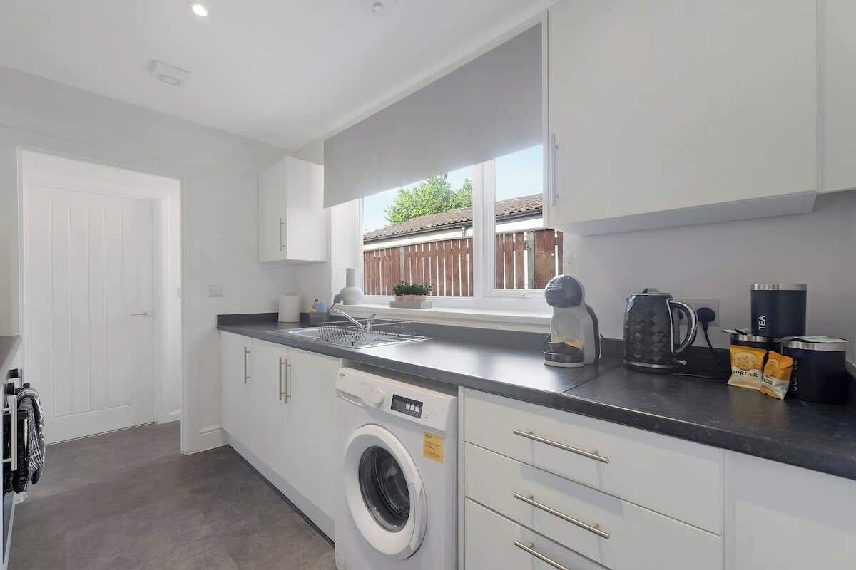 A modern kitchen with a built-in washing machine, a coffee maker, and a window with a view of a wooden fence.