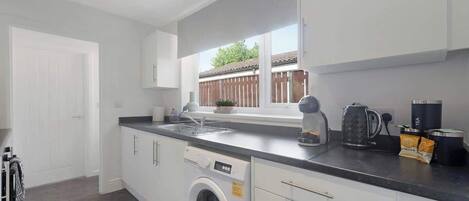 A modern kitchen with a built-in washing machine, a coffee maker, and a window with a view of a wooden fence.