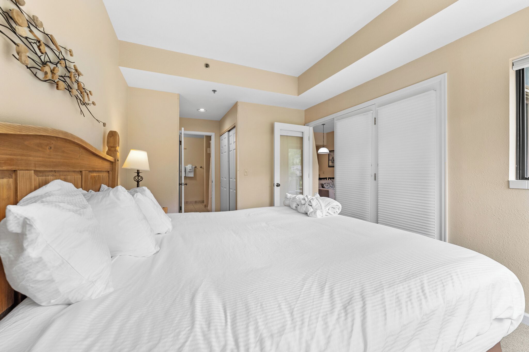 Una habitación de hotel con una cama grande, cabecero de madera, lámpara fijada a la pared y una puerta que da a un baño.