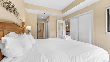 Una habitación de hotel con una cama grande, cabecero de madera, lámpara fijada a la pared y una puerta que da a un baño.
