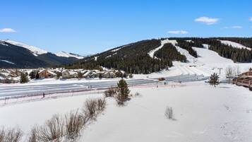 A snow-covered ski resort with multiple chalet-style buildings, a ski lift, and a clear blue sky.