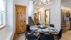 Comedor con una mesa redonda dispuesta para seis personas, rodeada de sillas negras, un candelabro y una puerta de madera.
