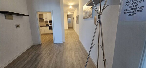 A hallway with a kitchen area visible through an open door, a metal ladder leaning against the wall, and a sign warning of police penalties for disturbances.