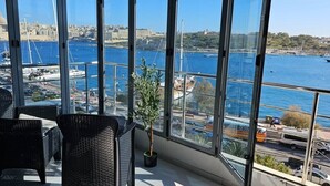 A balcony with wicker chairs and a potted plant, overlooking a harbor with boats and a cityscape. - Sea View Modern Apartment in Sliema Ferry 250 sqm (Tas-Sliema)