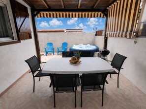 Une terrasse extérieure avec une table ronde, quatre chaises, un jacuzzi et des chaises bleues.