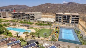 Un complesso residenziale con diversi edifici, una piscina, un campo da tennis e una zona verde con palme.