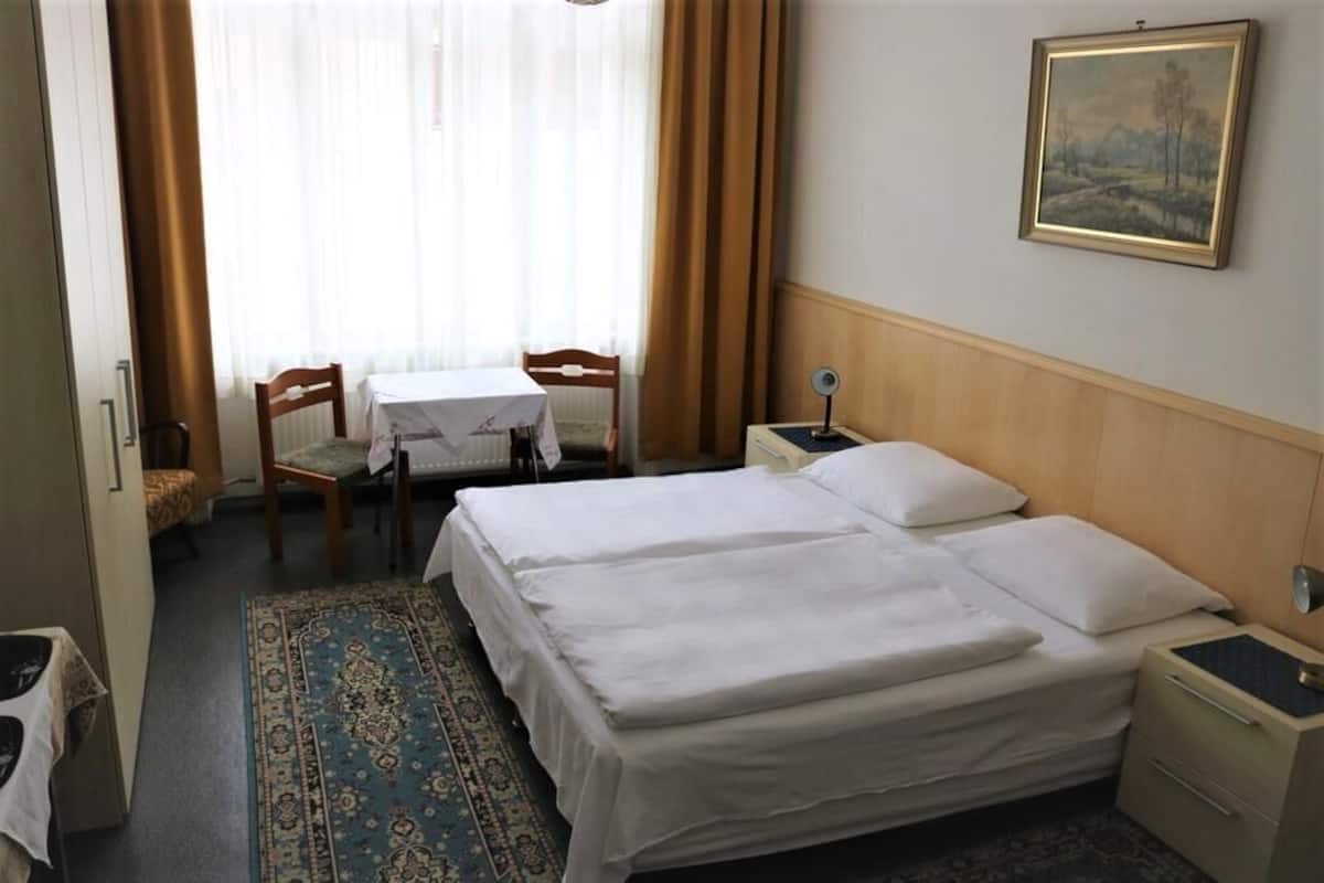 Una habitación de hotel con una cama, un escritorio con silla, una mesita de noche y un cuadro en la pared.