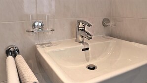 Ein Badezimmer mit einem weißen Waschbecken, einem chromfarbenen Wasserhahn und einer Seifenschale aus Glas.