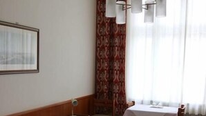 Ein Hotelzimmer mit zwei Betten, einem Tisch, Stühlen, einer Lampe und einem Fenster mit Vorhängen.