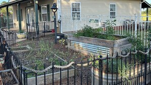 A two-story house with a green roof, a porch with a black metal fence, and a garden area with raised beds.