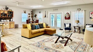 A spacious living room with a yellow sofa, a glass coffee table, and a dining area with wooden chairs and a cabinet.