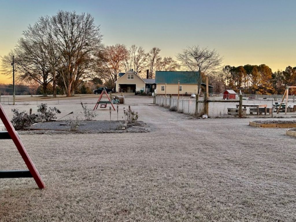 A rural property with a large open field, a swing set, a small house, and a barn.