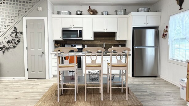 A modern kitchen with white cabinets, stainless steel appliances, a wooden dining table with four chairs, and a staircase leading to an upper level.