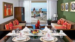 Uma área de refeições com uma mesa posta para quatro pessoas, vista para o oceano e uma varanda com duas pessoas.