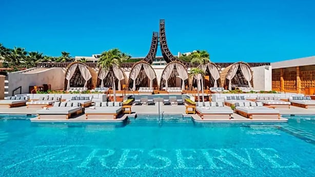 Piscina de resort com a palavra 'PRESERVE' escrita na água, rodeada por espreguiçadeiras e palmeiras.