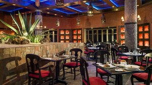 A restaurant with brick walls, red cushioned chairs, and tables set for dining.