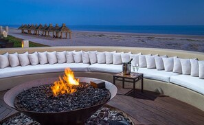 Uma área de estar à beira-mar com lareira, uma mesa com bebidas e vista para o oceano.