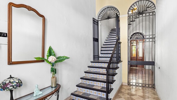 A staircase with black railings, a mirror on the wall, a vase with flowers, and a small Buddha statue. - Quiet Romantic Retreat: Walk Everywhere • King Bed • Historic Charm (San Juan)