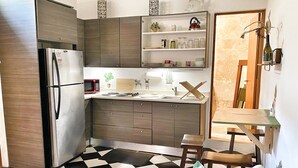 A compact kitchen with a refrigerator, microwave, and wooden cabinets. There is a dining area with a table and chairs, and a checkered floor. - Quiet Romantic Retreat: Walk Everywhere • King Bed • Historic Charm (San Juan)