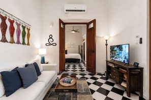 A hotel room with a checkered floor, a white sofa, a television, and a hallway leading to a bedroom. - Quiet Romantic Retreat: Walk Everywhere • King Bed • Historic Charm (San Juan)