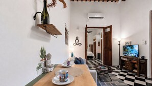 A dining area with a wooden table, a television, and a checkered floor. - Quiet Romantic Retreat: Walk Everywhere • King Bed • Historic Charm (San Juan)